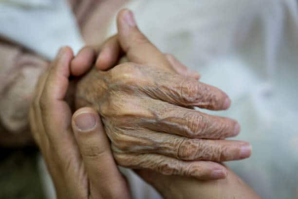 Aide-soignante qui tient les mains à une personne âgée en situation de perte d'autonomie
